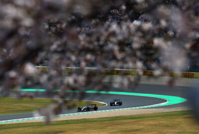 2026年F1日本大奖赛一练，两辆赛车驶过樱花映衬下的铃鹿赛道2号弯