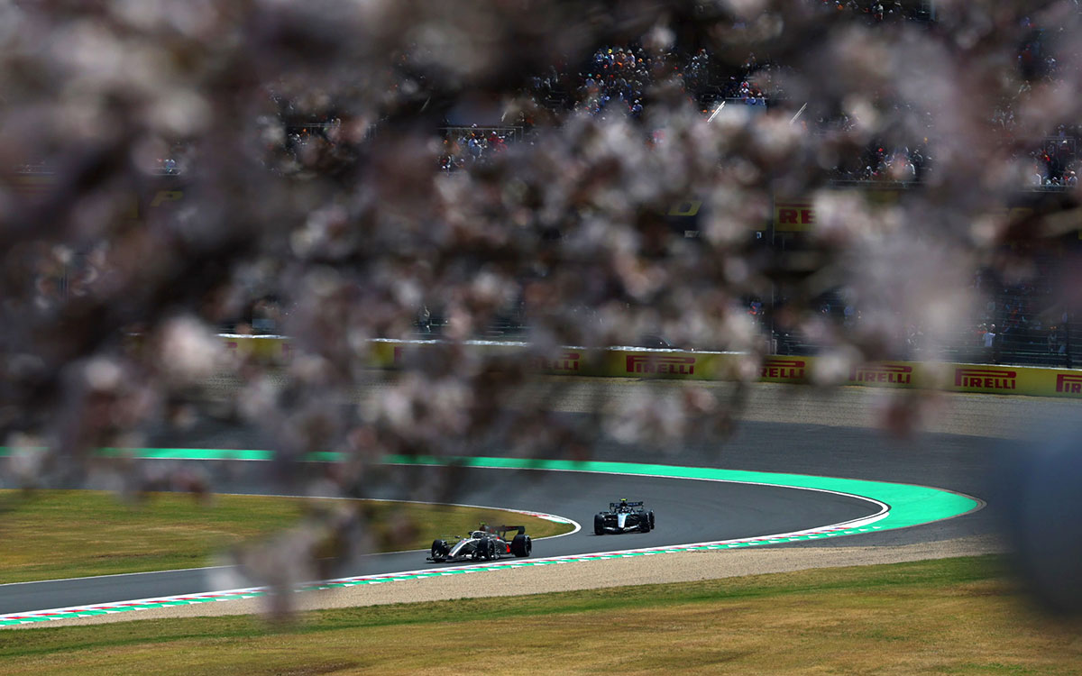 2026年F1日本大奖赛一练，两辆赛车驶过樱花映衬下的铃鹿赛道2号弯