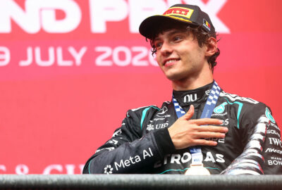 2026年F1比利时大奖赛：安东内利在斯帕领奖台上佩戴Pirelli领奖台帽，手抚FIA奖牌露出微笑