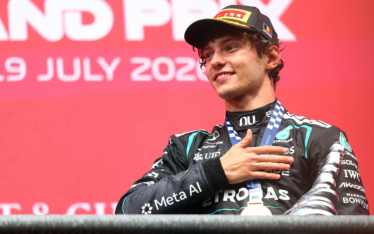 2026年F1比利时大奖赛：安东内利在斯帕领奖台上佩戴Pirelli领奖台帽，手抚FIA奖牌露出微笑