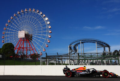 2023年F1日本大奖赛排位赛，维斯塔潘驾驶红牛RB19赛车行驶在铃鹿赛道维修区通道，背景为游乐园摩天轮