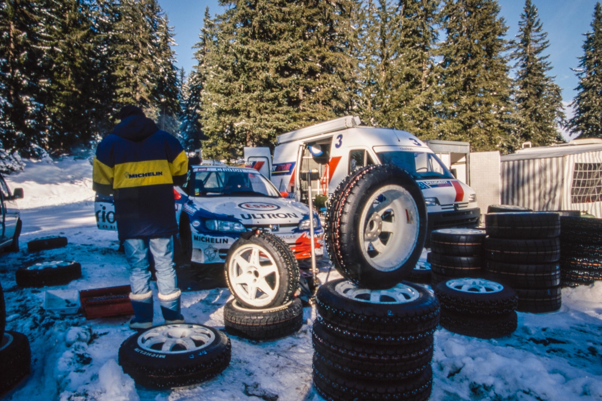 Personnel, tyres and cars in Peugeot's 306 service area at the 1998 Monte Carlo Rally.